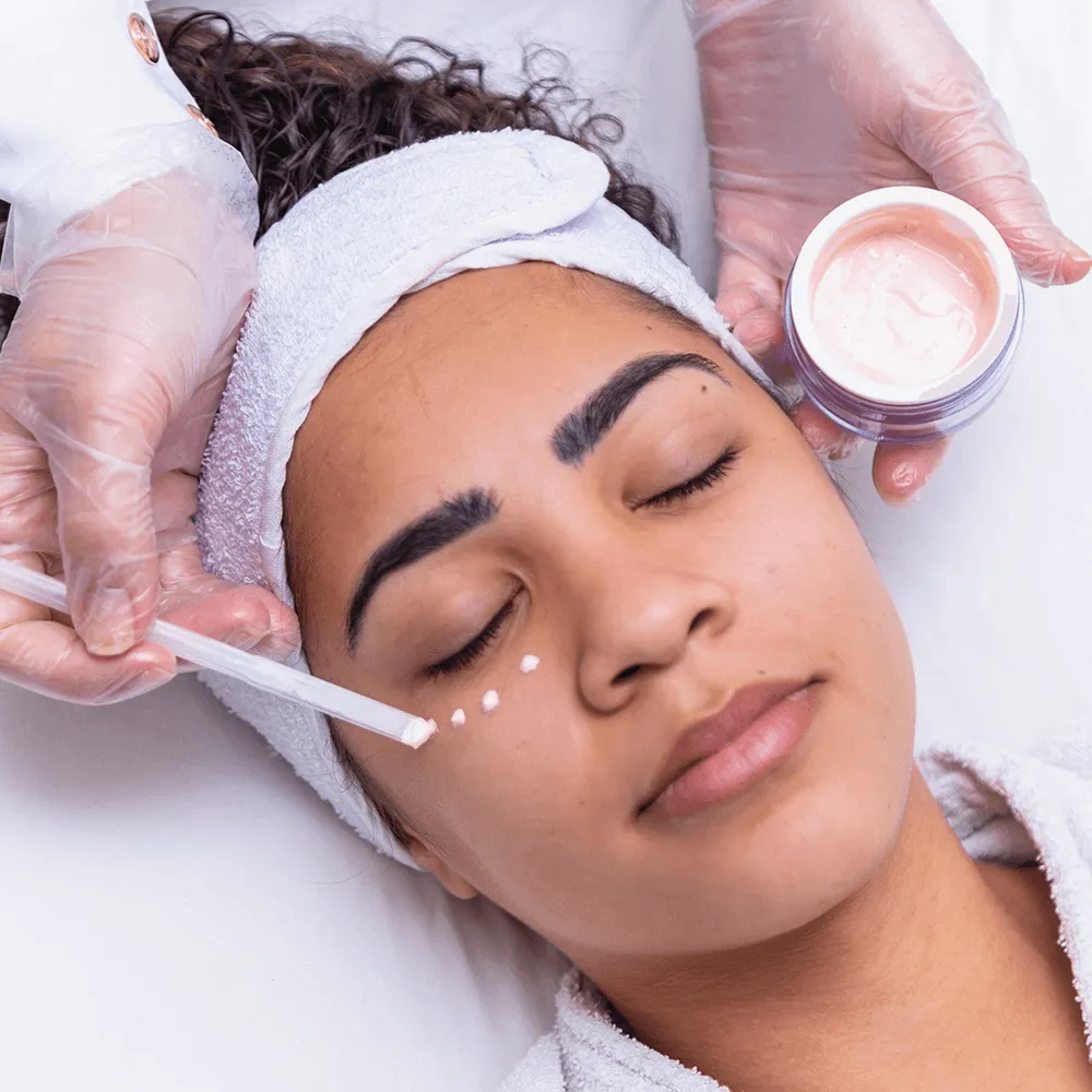 Woman receiving BioRePeel facial treatment with professional applying pink cream