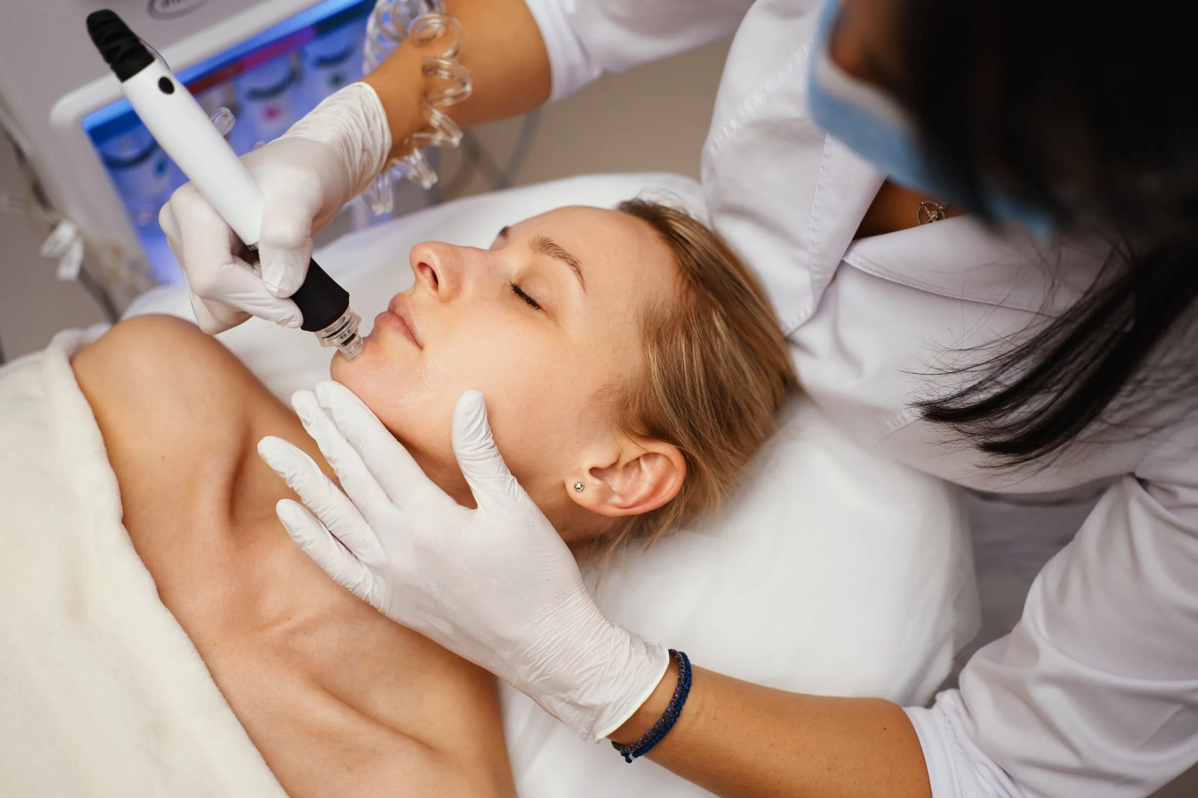 Aesthetician performing a microneedling procedure on a relaxed female client lying on a treatment bed in a skincare clinic.
