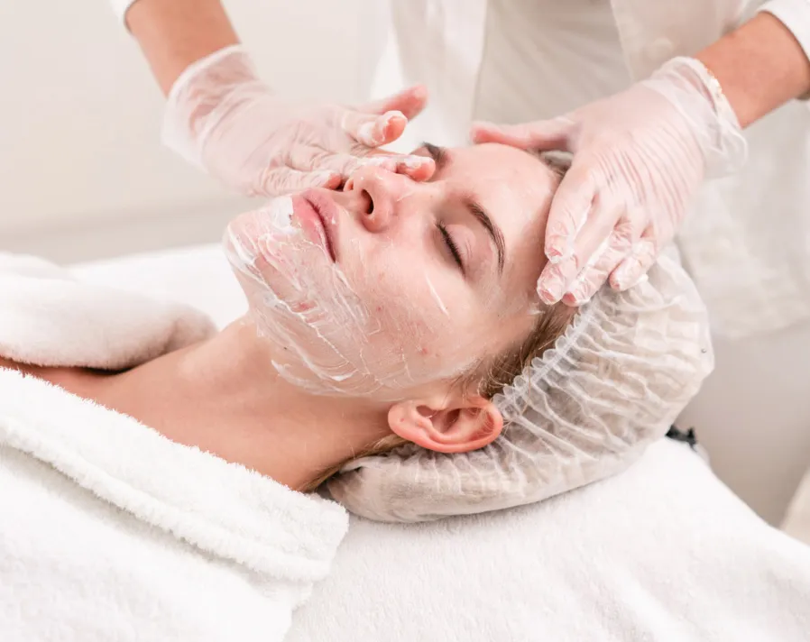 Woman receiving relaxing facial treatment with cream mask from professional in spa setting