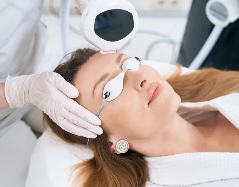 Woman receiving laser skin treatment at a dermatology clinic, wearing protective eyewear during the procedure.