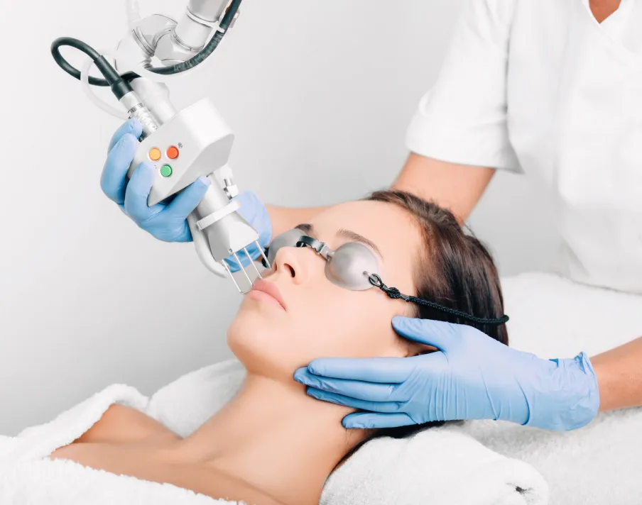 Woman receiving laser facial treatment with protective glasses from professional in clinical medspa setting