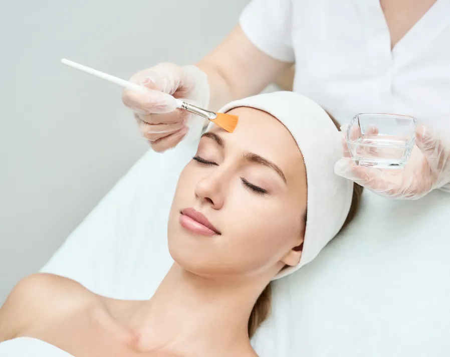 Woman receiving BioRePeel facial treatment from professional with applicator brush in clinical spa setting