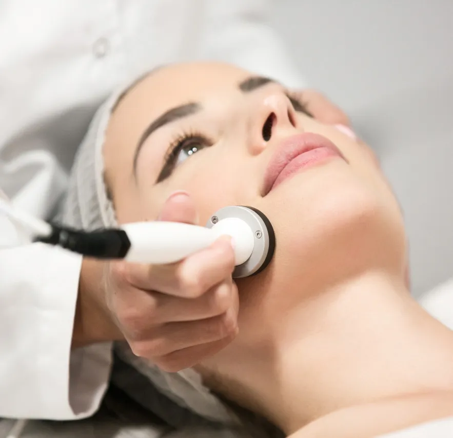 A woman receiving a facial skin treatment with a professional handheld device in a dermatology or medical spa setting.