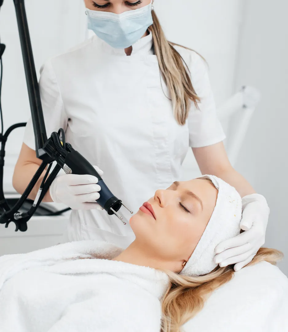 Professional performing laser or light-based facial treatment on woman in modern dermatology clinic