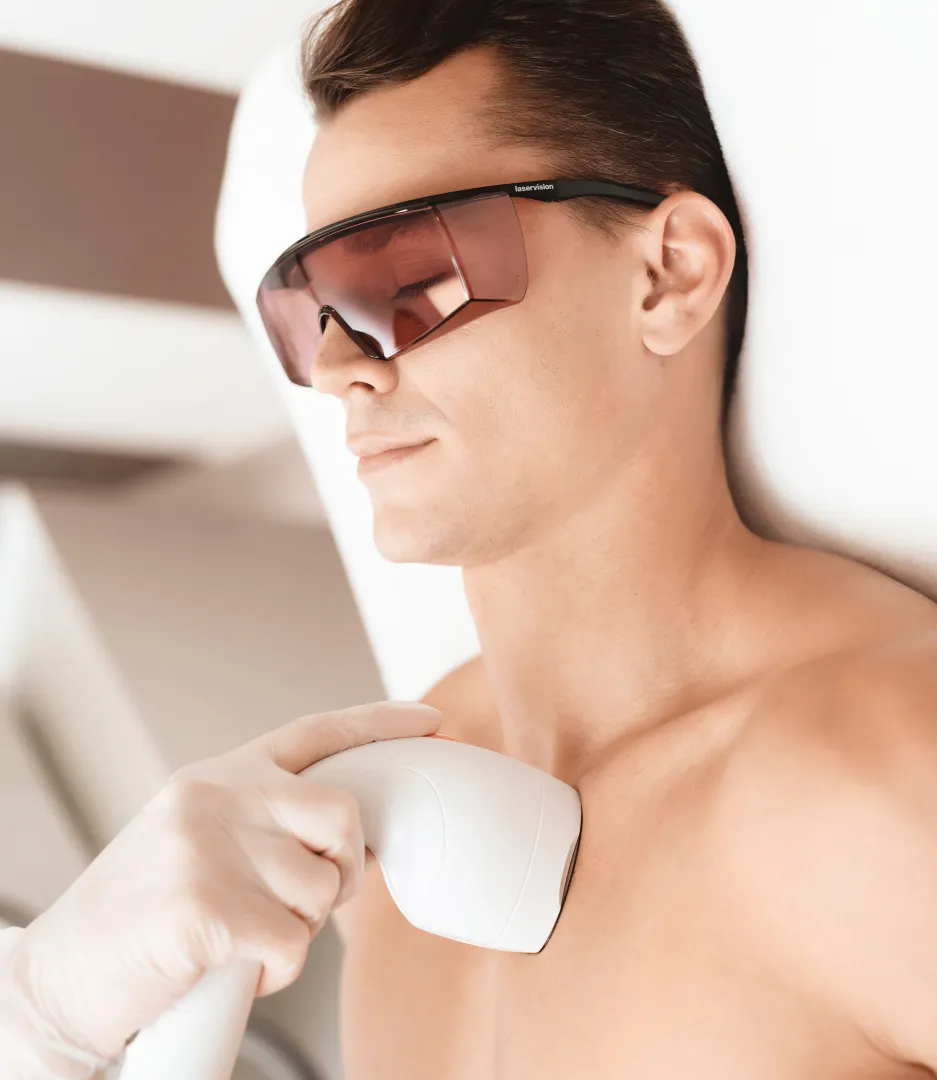 A man wearing protective glasses receiving a laser hair removal treatment on his chest at a dermatology clinic.