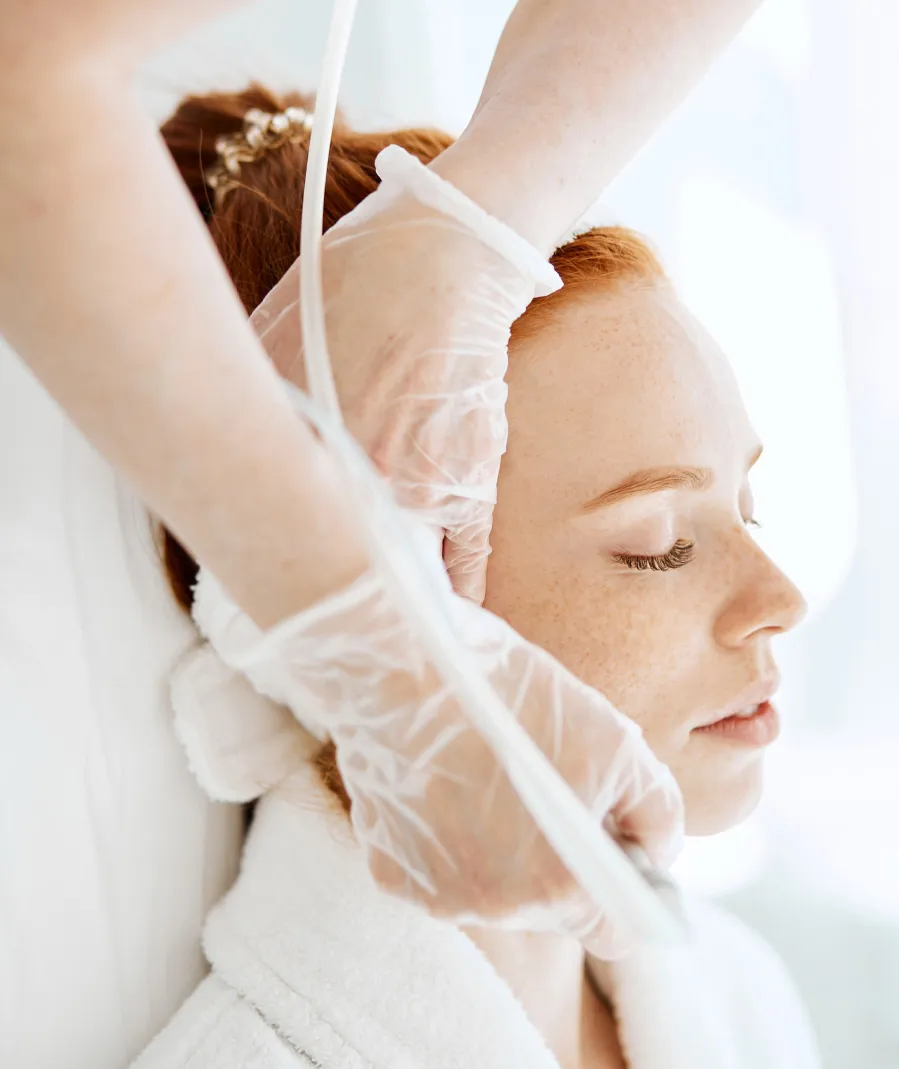 Red-haired woman receiving facial treatment with handheld device from professional