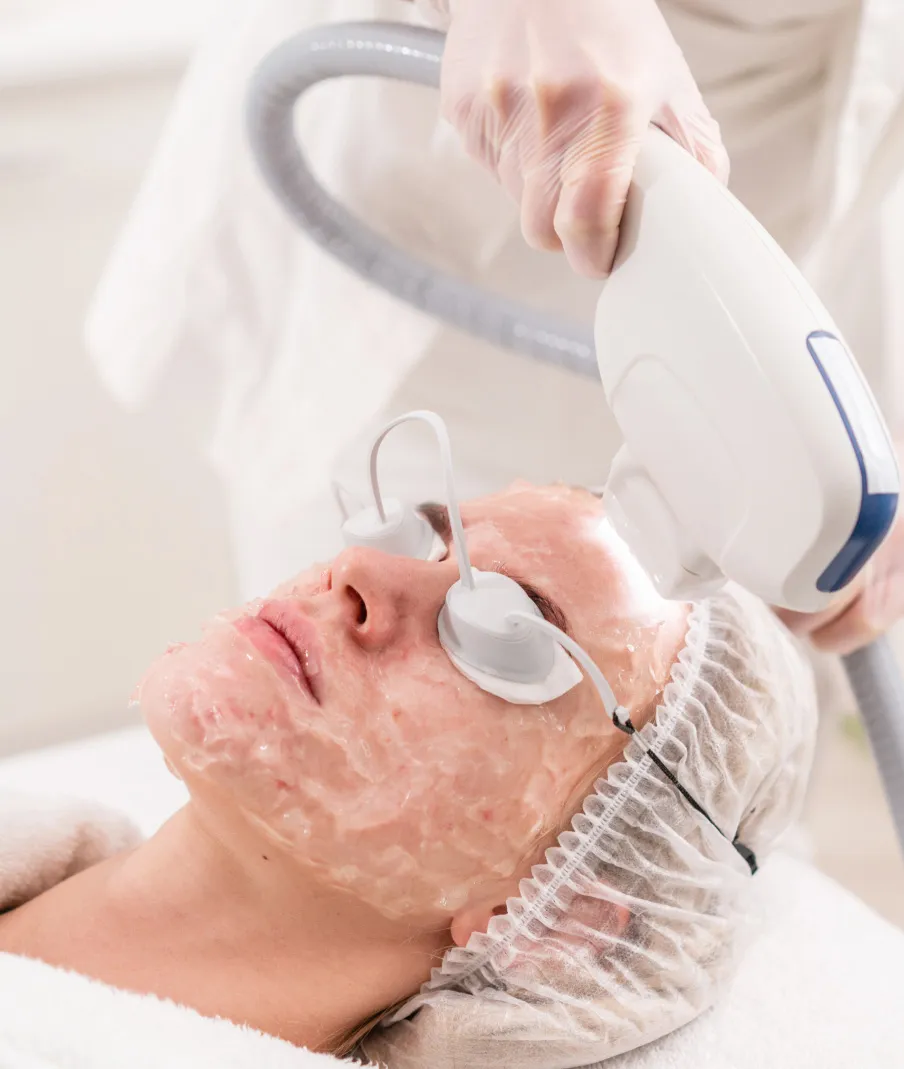 Woman receiving laser facial treatment with protective goggles and gel mask in clinical spa setting